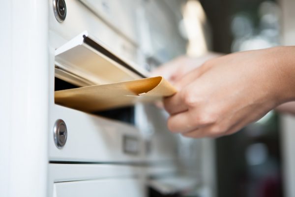 Hand, die Brief in Briefkasten einwirft Frau, die Brief in Briefkasten einwirft
